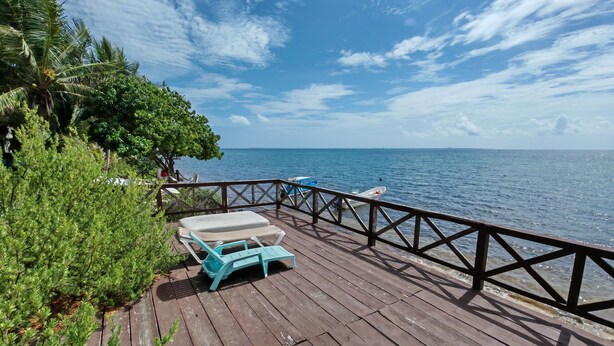 Une terrasse en bois avec deux chaises longues bleu clair et une petite table, donnant sur une mer calme.