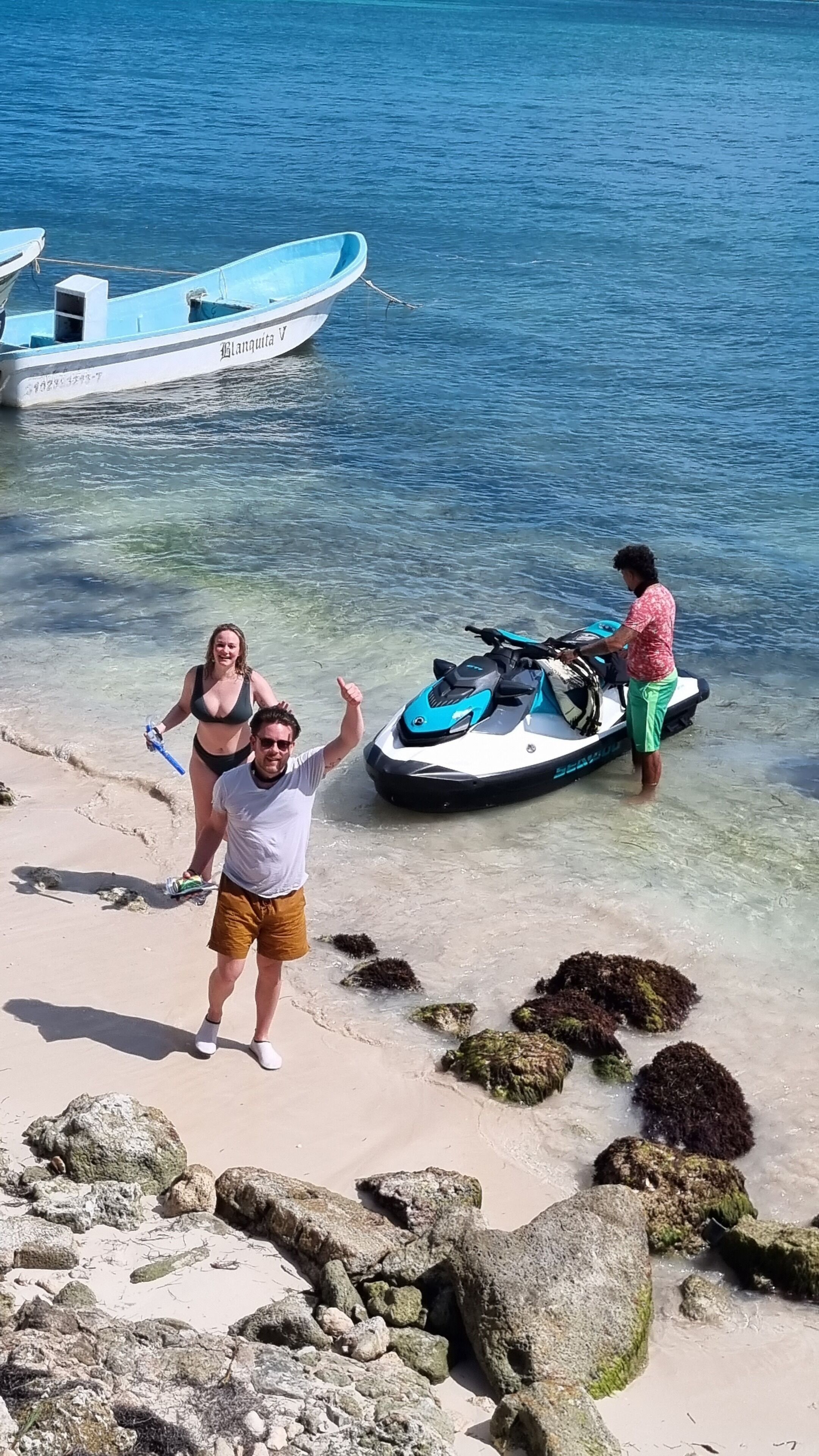 Une scène de plage avec un jet ski, un bateau et un paysage rocheux.