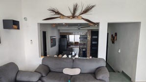 Un salon avec un canapé gris, une table basse sur laquelle se trouvent une boîte et une bouteille, et une branche décorative placée au-dessus du canapé.