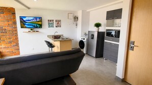 A modern living room with a sofa, a television, and a kitchen area with appliances. - Cold AC fast Wi-Fi great location  (Medellín)