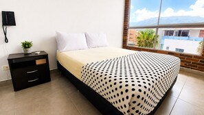 A bedroom with a bed, a nightstand, a potted plant, and a window with a view of buildings and mountains. - Cold AC fast Wi-Fi great location  (Medellín)