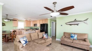 A spacious living room with two beige sofas, a dining area, and a kitchen with wooden cabinets.