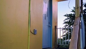 A wooden staircase leading to a door with a blue frame, a metal railing, and a yellow wall. - BioBay Inn Apt C - Cute Tiny Studio w/wifi & AC Near Malecon, Sun Bay (Vieques)