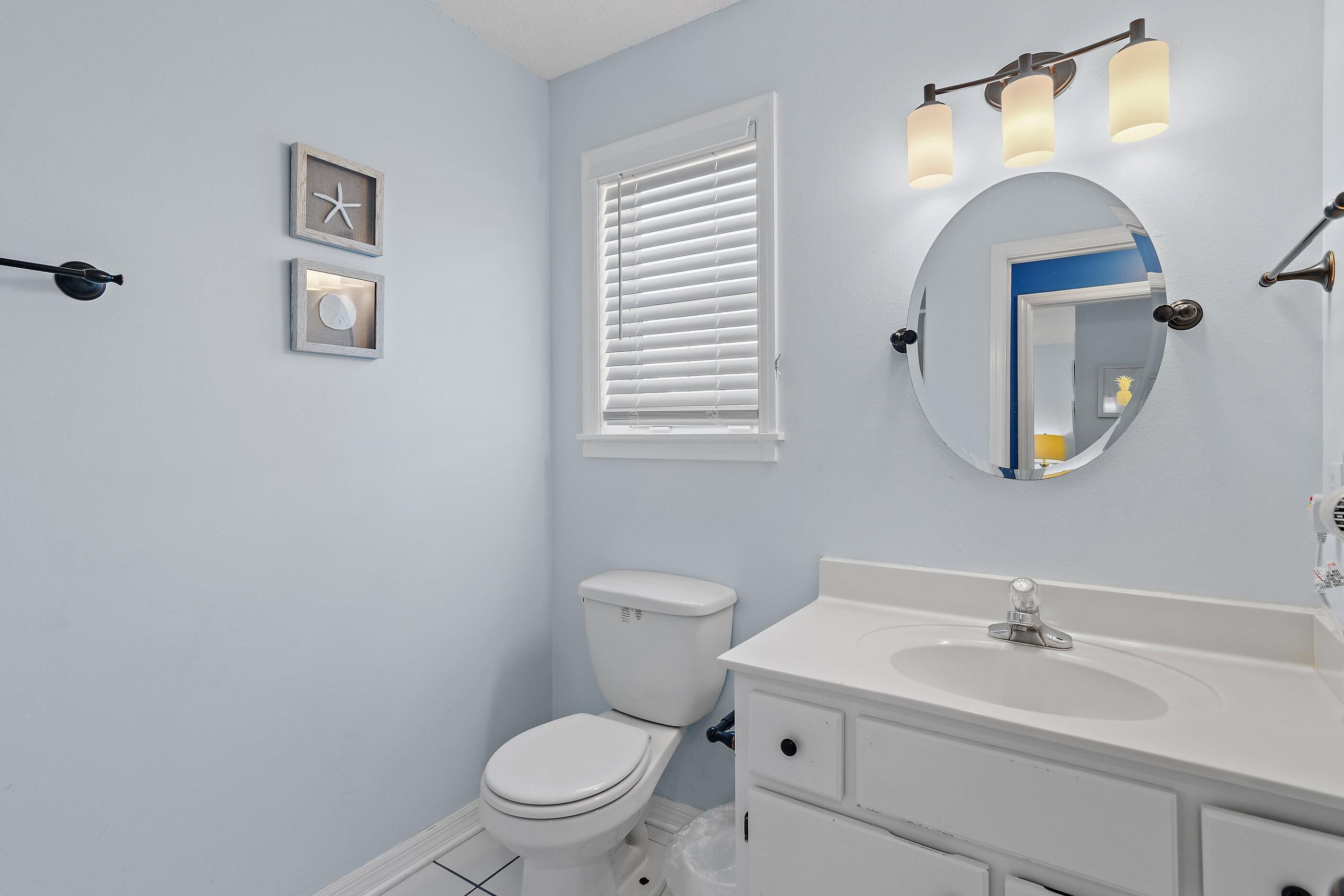 A bathroom with a toilet, sink, mirror, and wall-mounted lights.