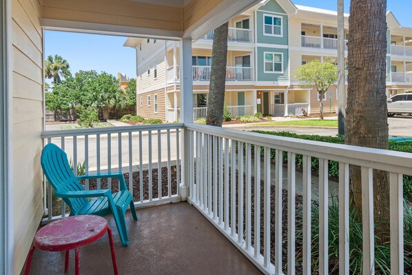 Un balcon abrité avec des balustrades blanches, deux fauteuils Adirondack turquoise et une petite table rouge.