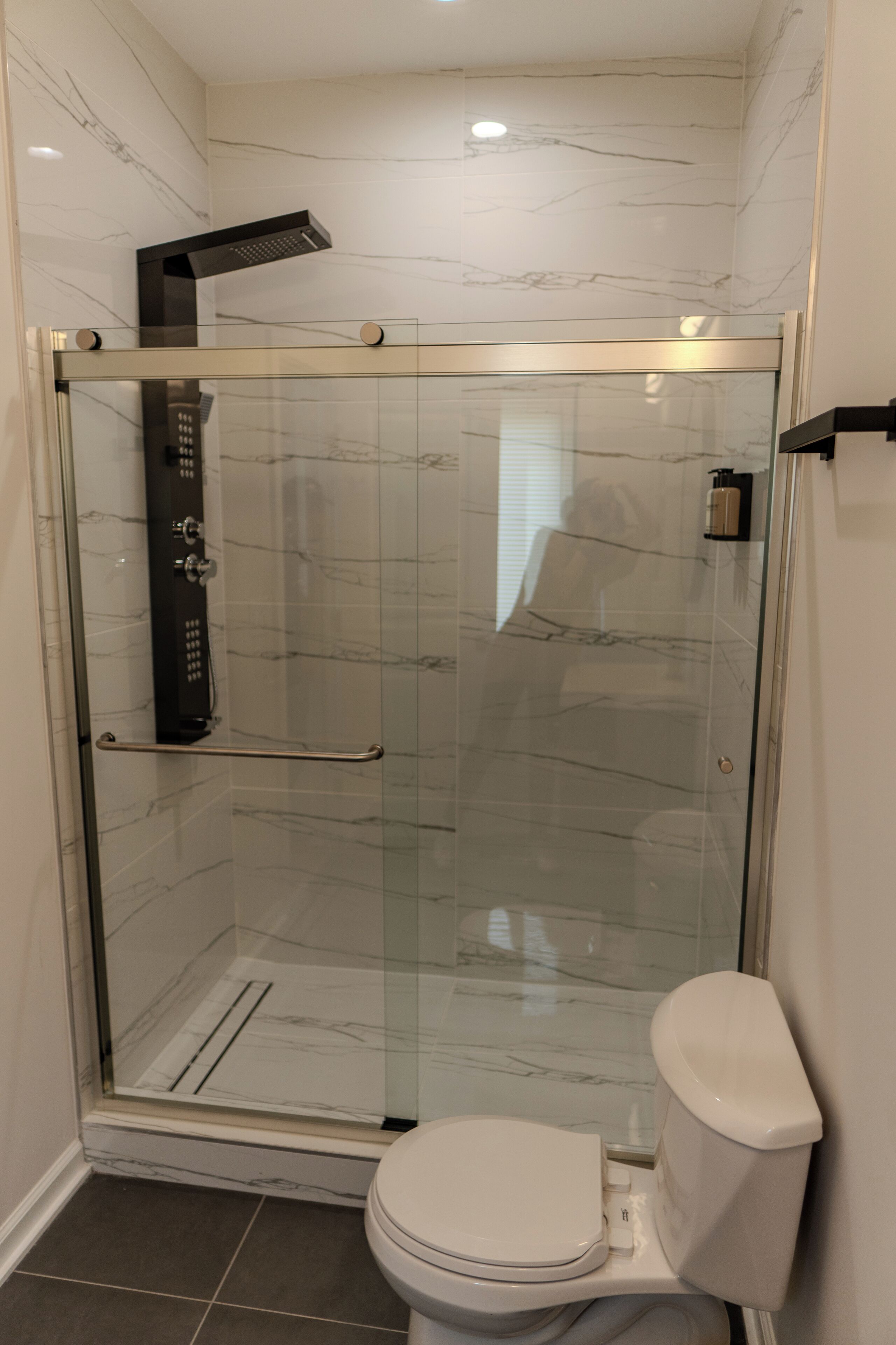 Une cabine de douche fermée par des parois en verre, dotée d’un pommeau de douche à main, d’une porte en verre et de toilettes blanches.