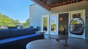Une terrasse extérieure avec un canapé bleu, deux tables rondes et un fauteuil suspendu.