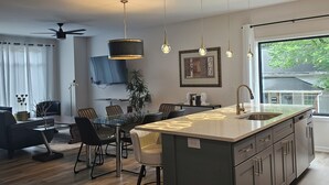 Une cuisine moderne dotée d’un îlot central, de luminaires suspendus, d’un ventilateur de plafond et d’un coin repas avec des chaises et une table.