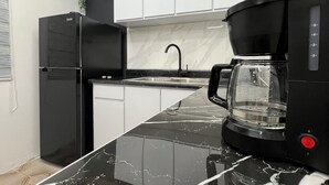 A modern kitchen with black cabinets, a marble countertop, a coffee maker, and a sink.