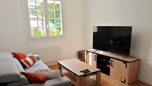 A modern living room with a grey sofa, a coffee table, and a TV on a wooden cabinet. - Les Chouans - Holiday home (Les Sables-d´Olonne)