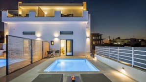 Un edificio moderno con piscina en la azotea, mobiliario exterior y una entrada bien iluminada.