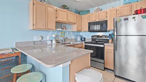 A modern kitchen with wooden cabinets, a stainless steel refrigerator, a microwave, and a stove. - Summerspell 303 (Miramar Beach)