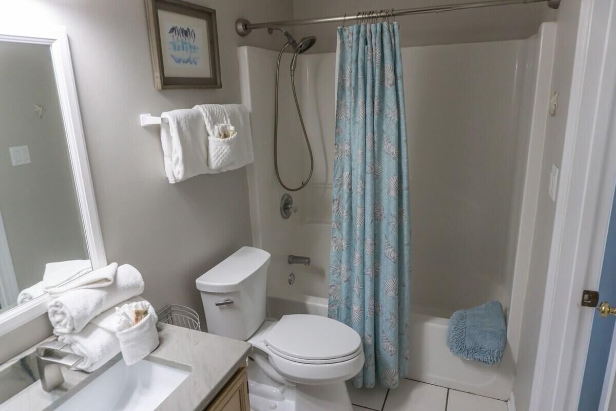 A bathroom with a toilet, sink, and shower. There are towels on the wall and a shower curtain.