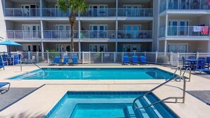 A pool area with two pools, lounge chairs, and a multi-story building with balconies. - Summerspell 303 (Miramar Beach)