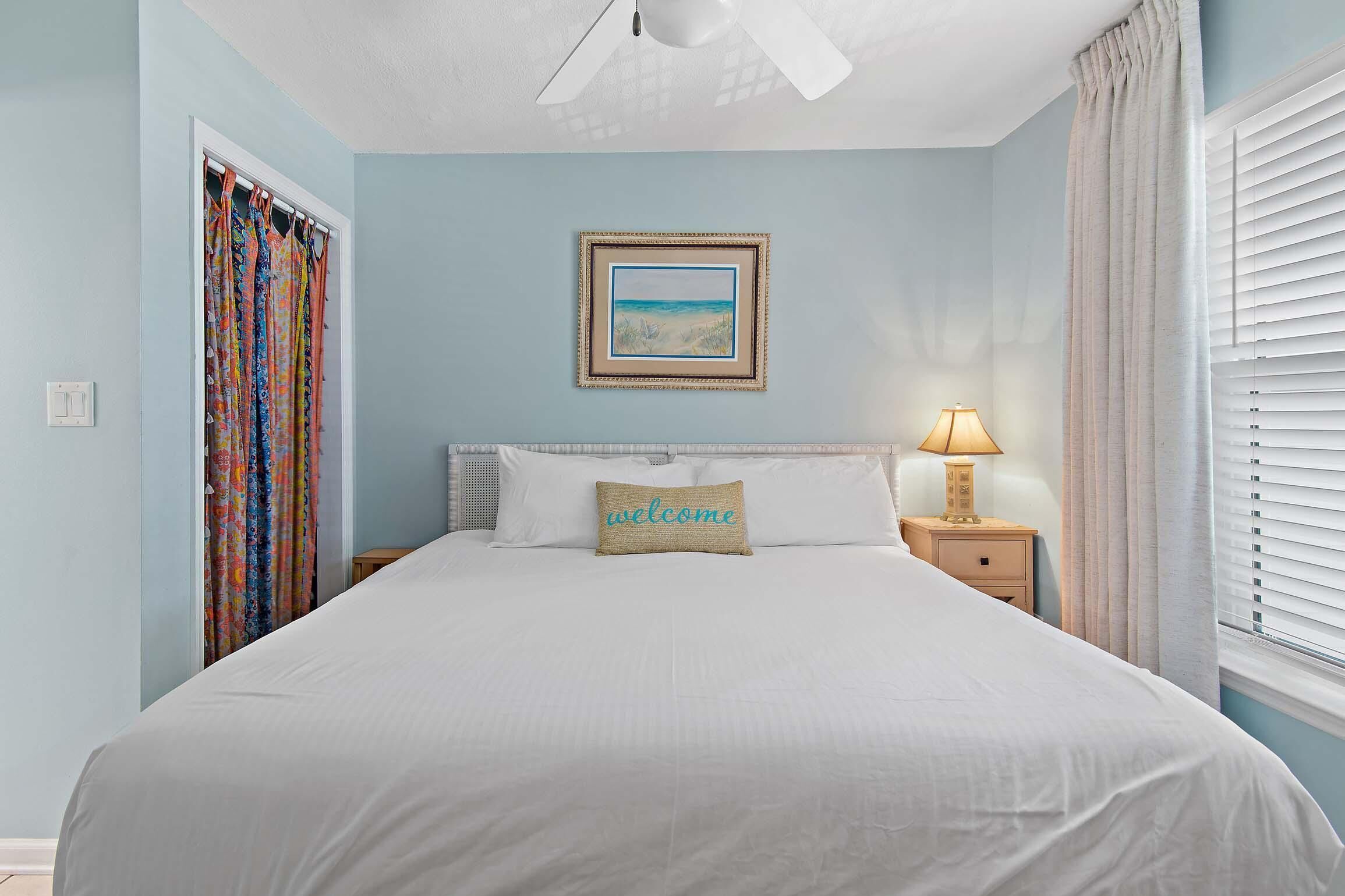 A bedroom with a bed, a nightstand, a lamp, a framed picture on the wall, and a window with curtains.