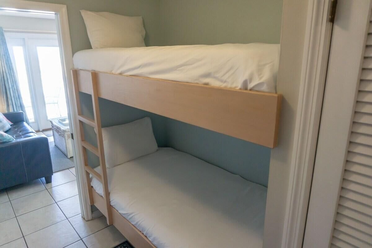A bunk bed with a ladder, a small table, and a chair in a room with a tiled floor.