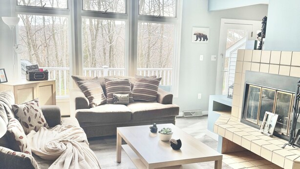 A modern living room with a large window, a fireplace, and a cozy seating area.