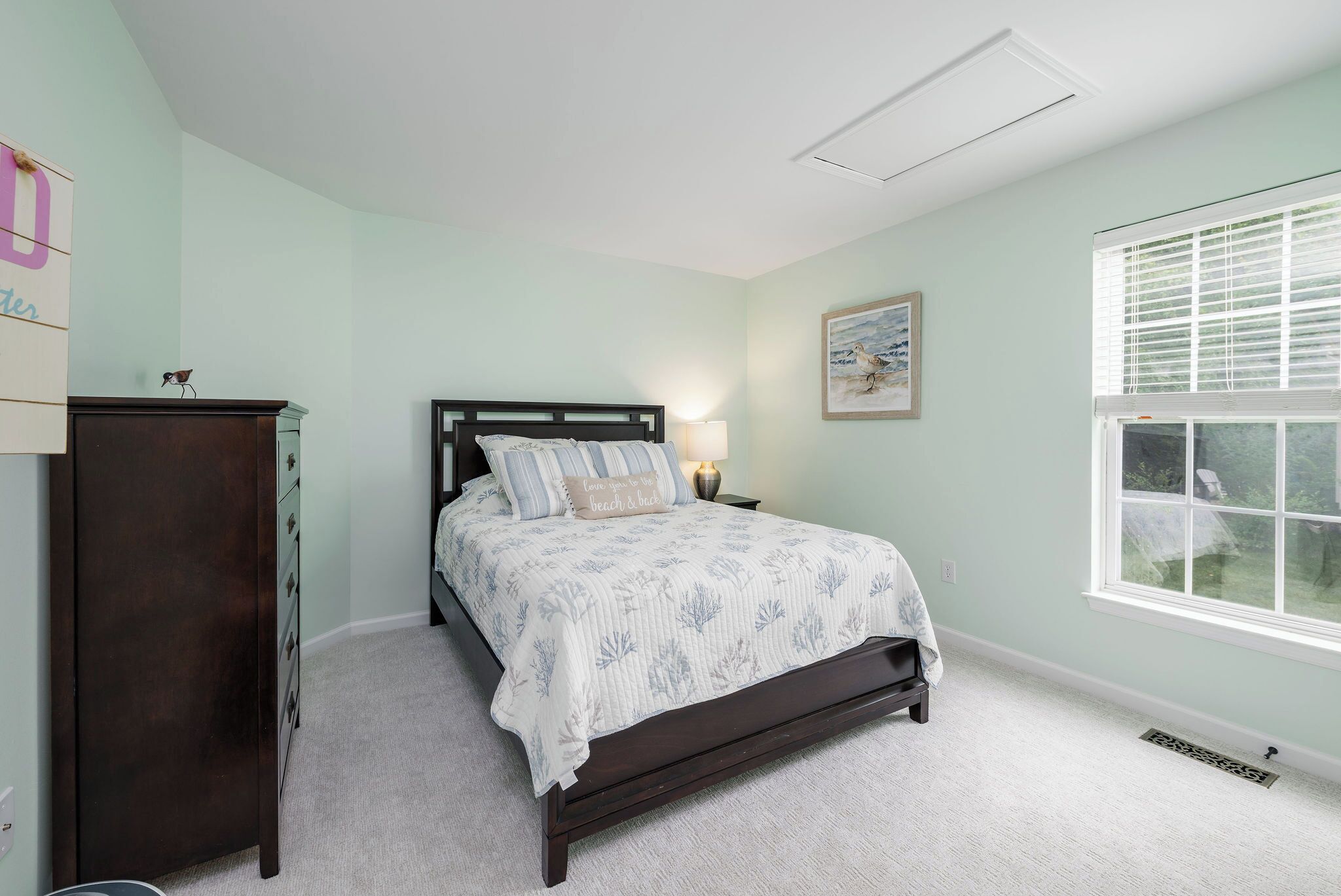 A bedroom with a bed, a dresser, a nightstand, a window, and a painting on the wall.