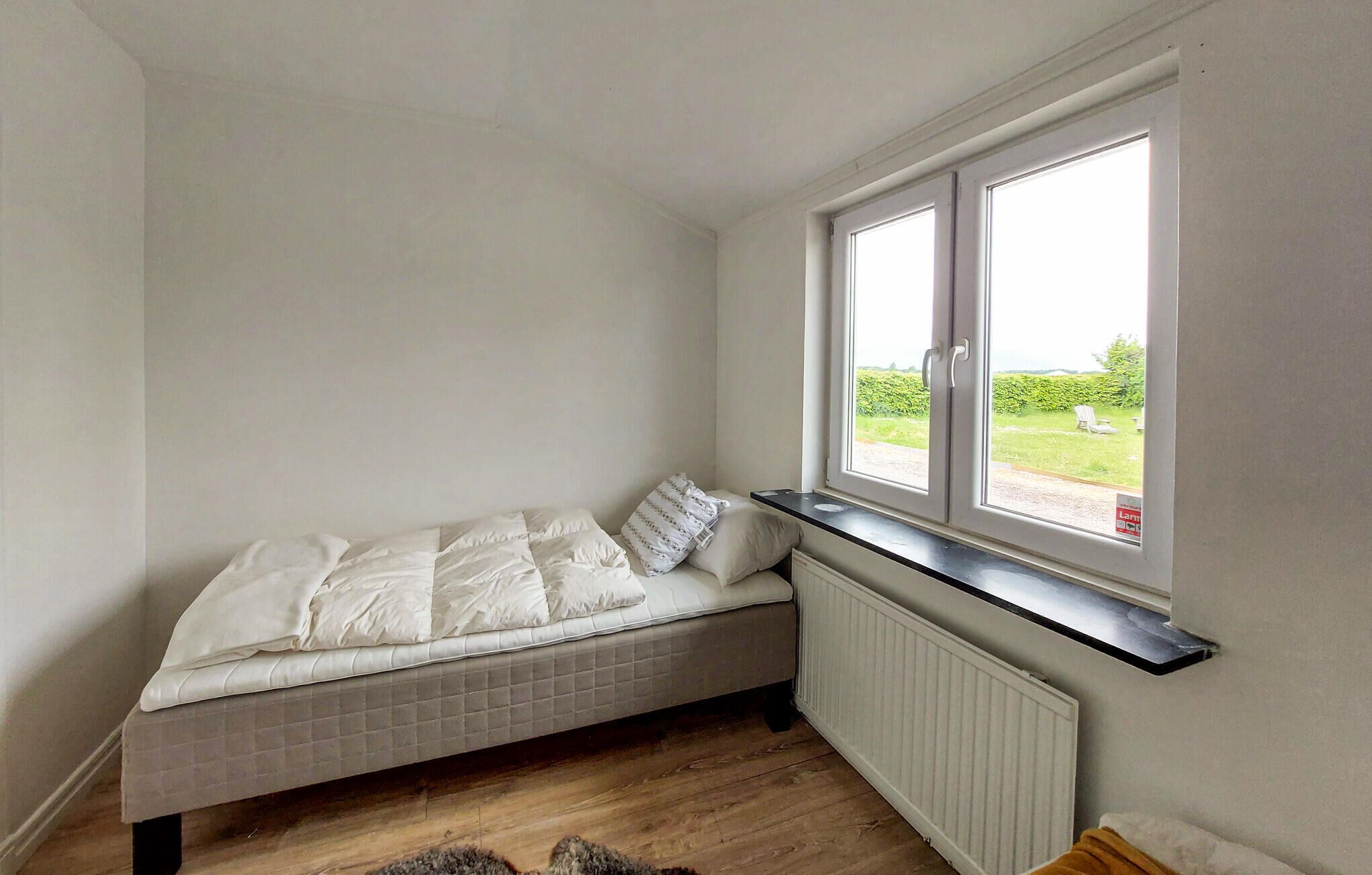 A small, cozy room with a single bed, a radiator, and a window overlooking a garden.