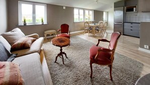 A spacious living room with a sofa, a coffee table, and two red chairs. There is a dining area with a table and chairs in the background. - 2 bedroom beautiful home in Fleninge (Fleninge)