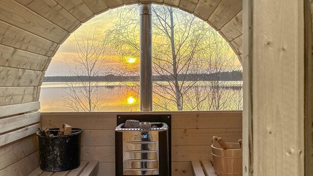 A wooden cabin with a bench, a sauna, and a view of a sunset over a lake. - Gorgeous home in Ryd with sauna (Ryd)