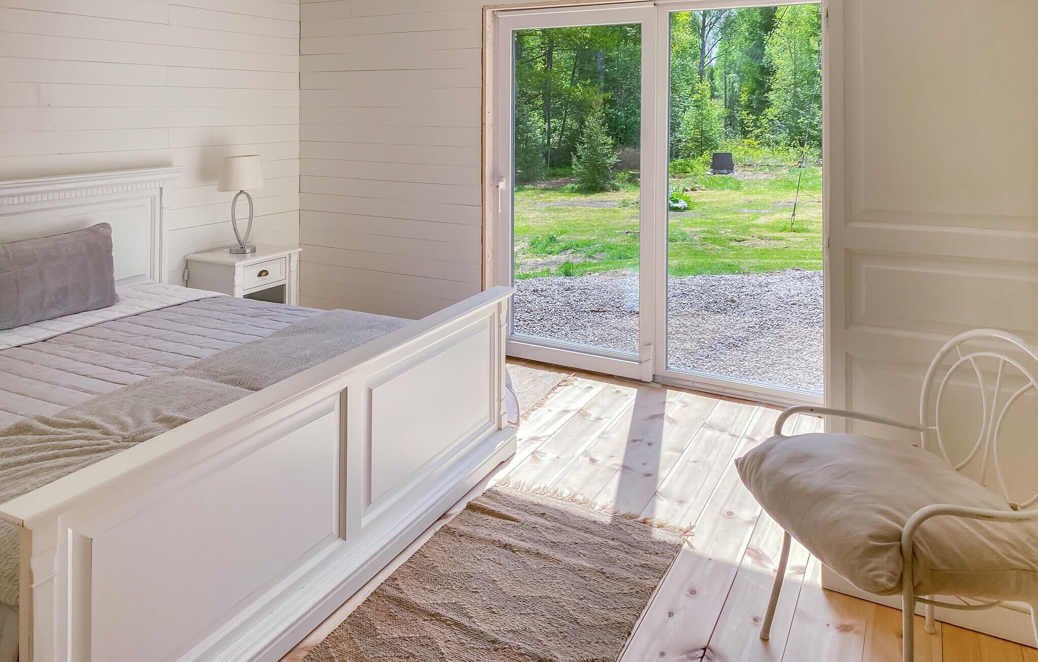 Une chambre à coucher avec un lit, une table de chevet, une lampe et une vue sur un jardin, visible à travers une porte vitrée.