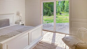 A bedroom with a bed, bedside table, lamp, and a view of a garden through a glass door. - Gorgeous home in Ryd with sauna (Ryd)