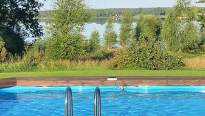 A swimming pool with metal ladders, surrounded by trees and a view of a lake. - Gorgeous home in Ryd with sauna (Ryd)
