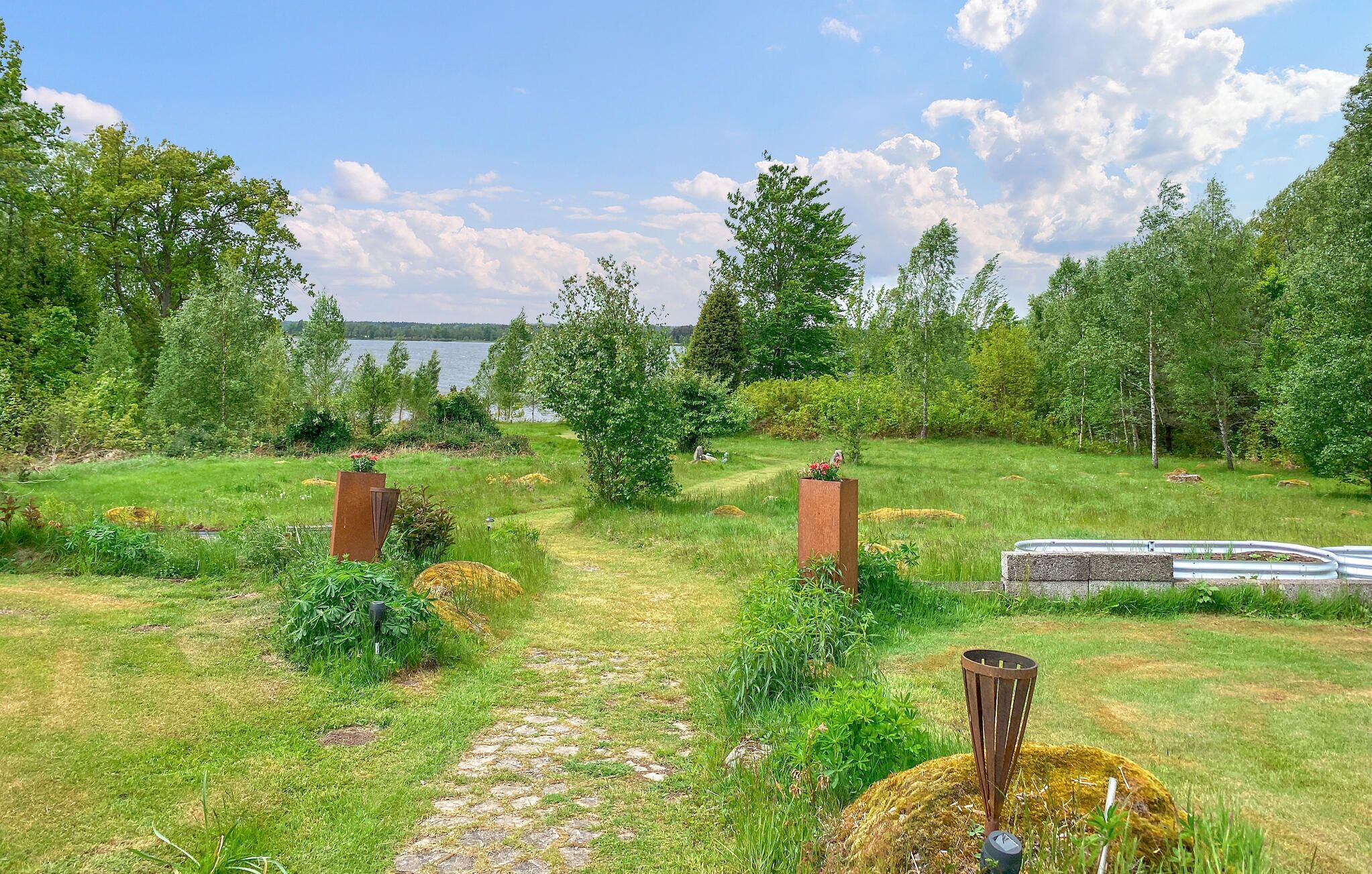 Un sentier de jardin qui mène à un plan d’eau, entouré d’arbres et de verdure.