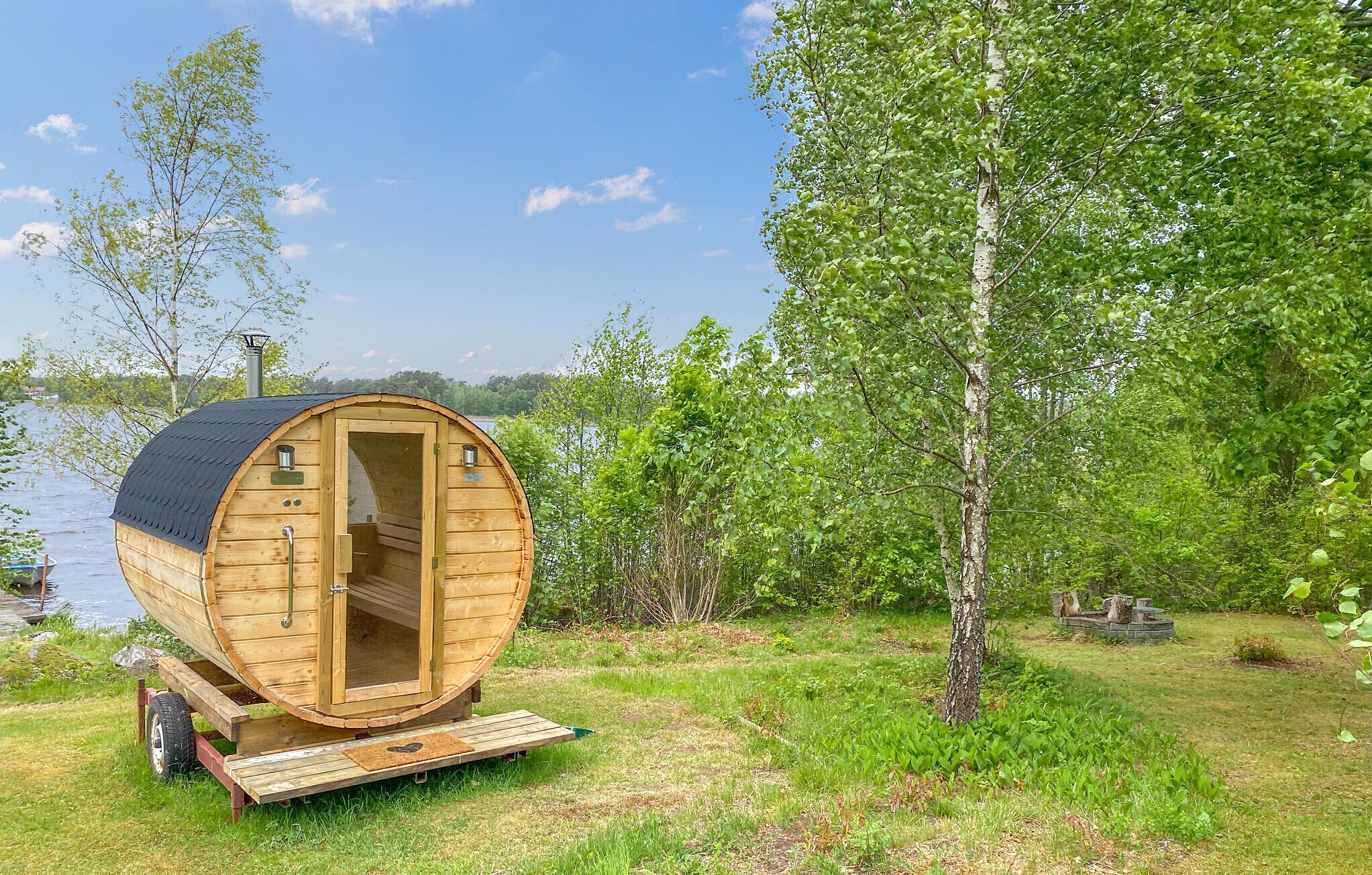 Une cabane en bois avec un toit incurvé, une porte et des fenêtres, située dans une zone herbeuse près d’une étendue d’eau.