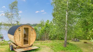 A wooden cabin with a curved roof, a door, and windows, situated on a grassy area near a body of water. - Gorgeous home in Ryd with sauna (Ryd)