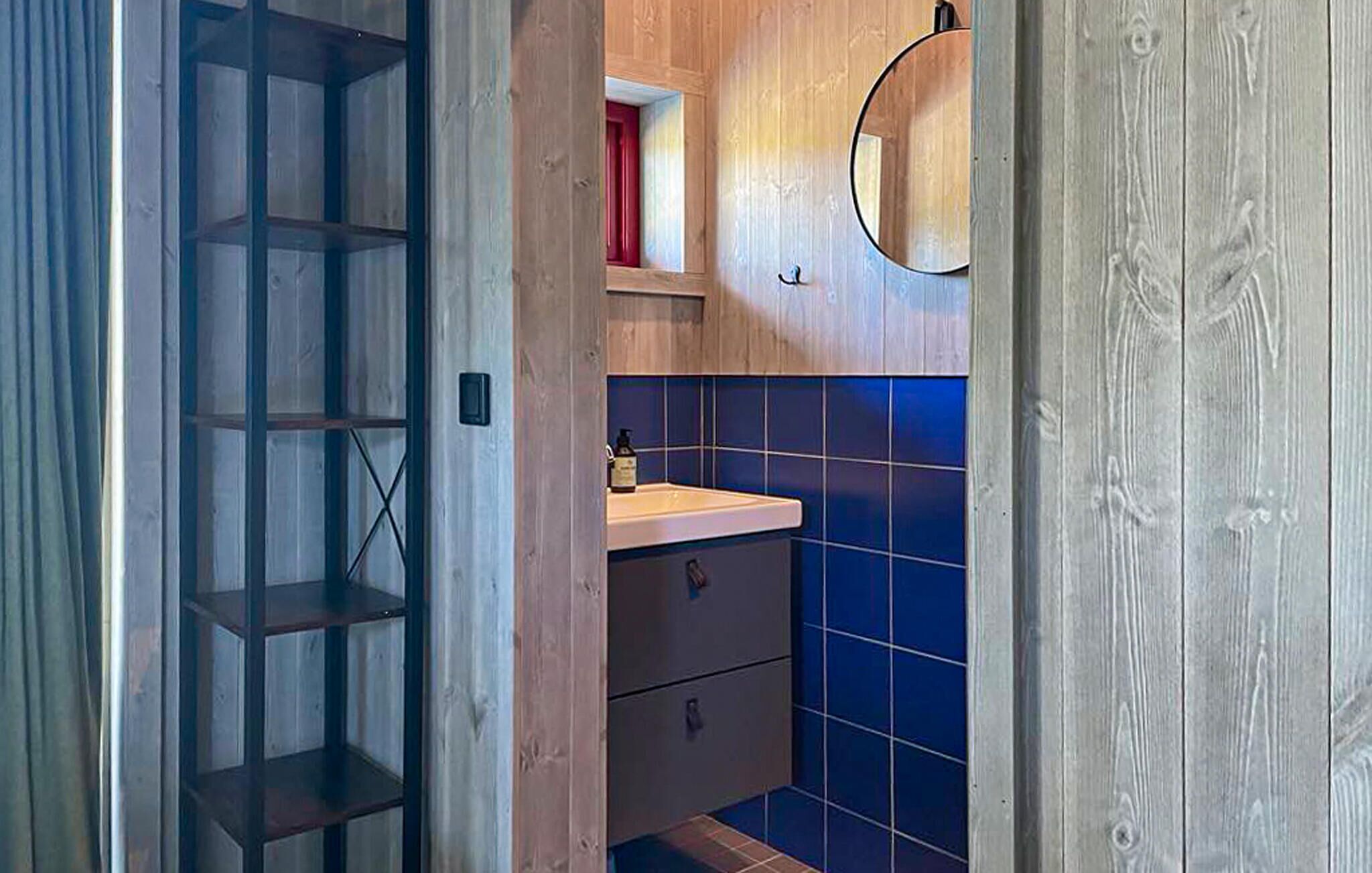 Une salle de bain avec une porte en bois, une étagère sur laquelle se trouve un objet rouge, un miroir et des carreaux bleus.