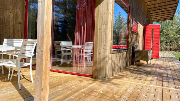 A wooden deck with outdoor seating and large sliding glass doors. - 2 bedroom cozy home in Lärbro (Lärbro)