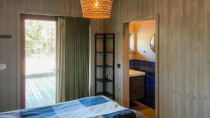 A bedroom with a bed, a window with curtains, a shelf, and a bathroom visible through an open door. - 2 bedroom cozy home in Lärbro (Lärbro)