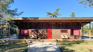 A rustic cabin with a wooden exterior, a red door, and two windows with red curtains. - 2 bedroom cozy home in Lärbro (Lärbro)