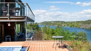 A wooden deck with a pool, a glass balustrade, wicker chairs, and a table.
