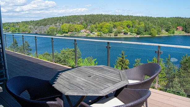 A deck with a table and chairs overlooking a lake with a forested shoreline.
