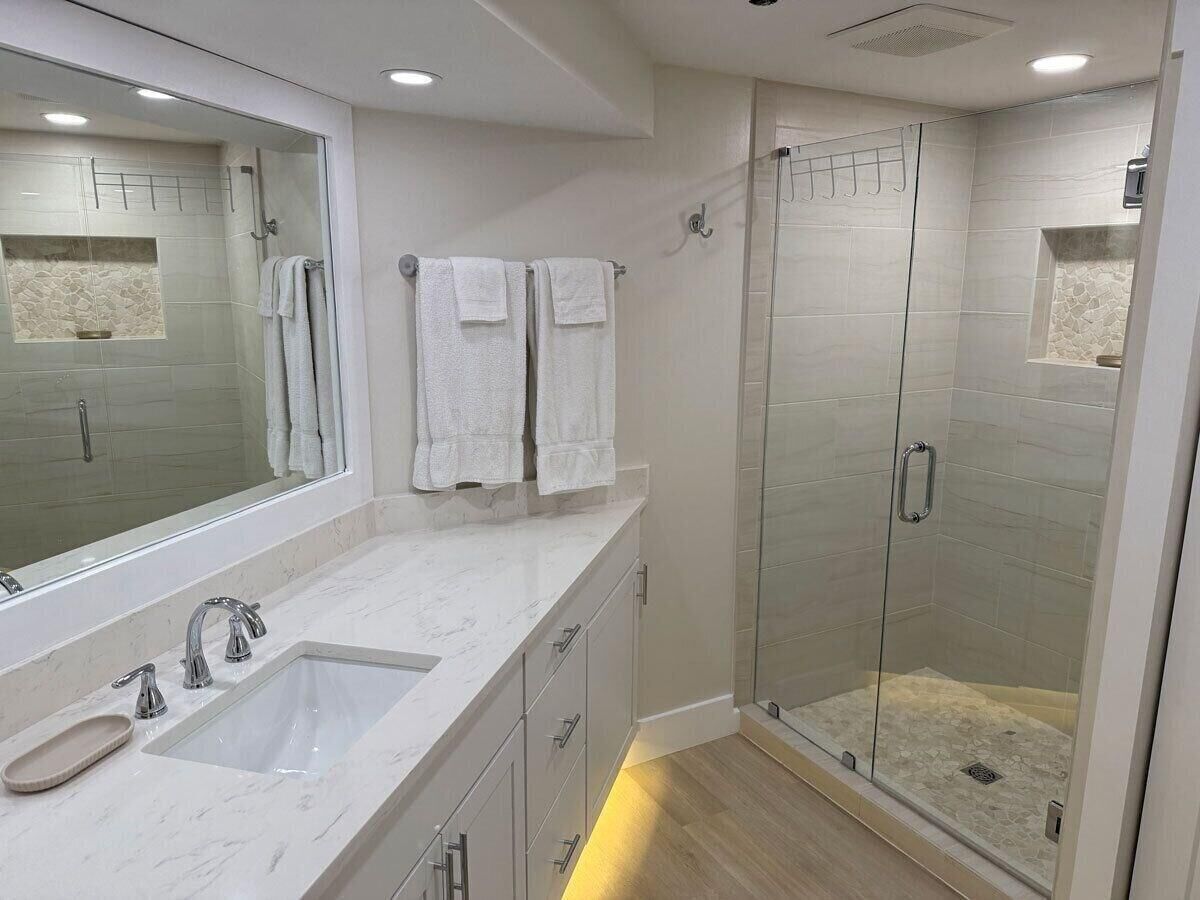 Ein modernes Badezimmer mit einer gläsernen Dusche, einem großen Spiegel und einer Marmorplatte.