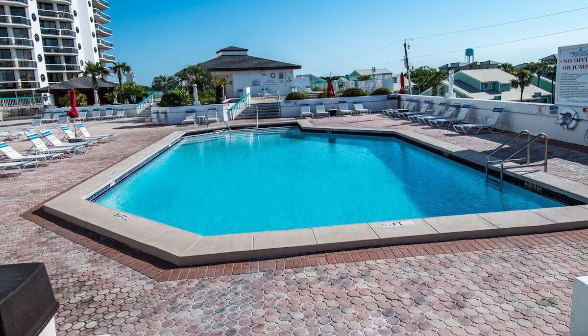 A rectangular swimming pool with a tiled deck, surrounded by lounge chairs and umbrellas.