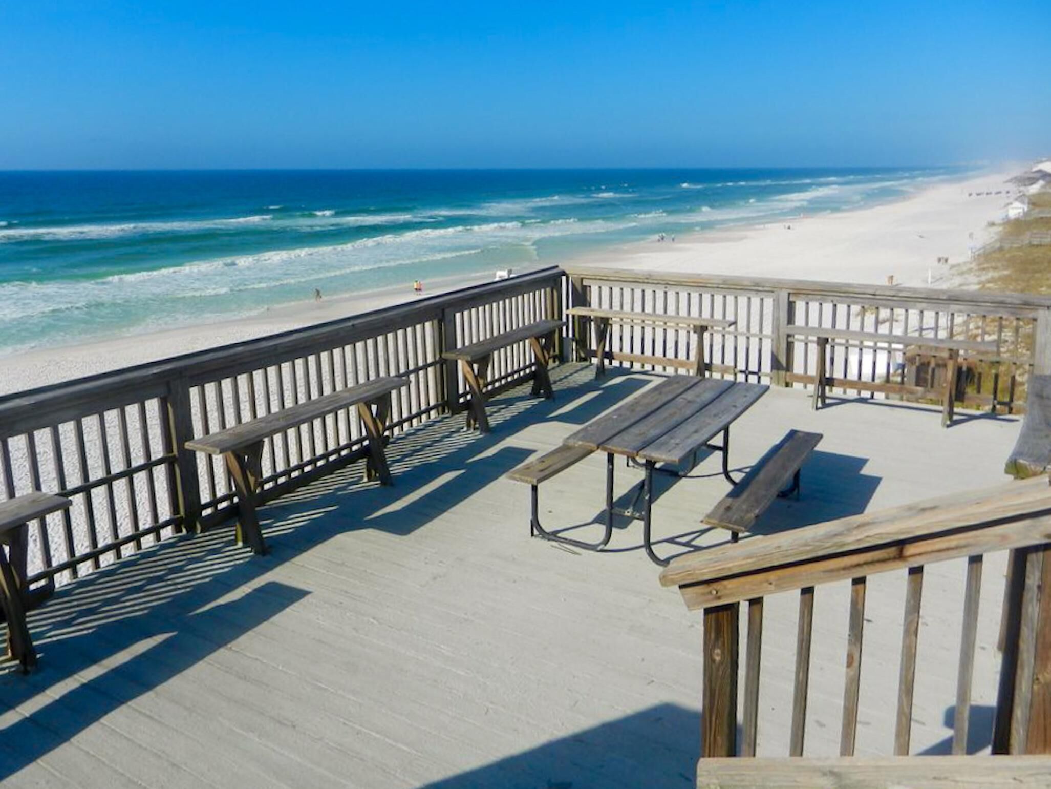 A wooden deck with picnic tables overlooking a beach.