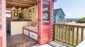 Une cabane chaleureuse avec une terrasse en bois, un petit coin cuisine et un banc agrémenté de coussins.