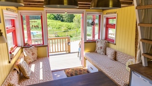Un intérieur chaleureux avec un banc en bois servant de siège, une petite table et une vue sur un jardin, visible à travers une porte.