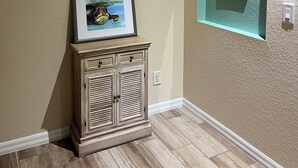 A hallway with a wooden cabinet, a framed picture, and a wall-mounted light switch.