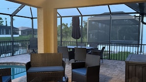 An outdoor patio area with wicker furniture, a ceiling fan, and a view of a swimming pool and houses in the background.