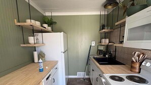A kitchen with a white refrigerator, stove, and microwave. There are wooden shelves with dishes and a plant. The floor is tiled, and the walls are green. - The Clover Cottage - Rolla's St.Pat's Themed house near S&T, Acorn Trail & more! (Rolla)