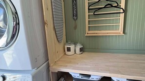 A compact laundry area with a washing machine, drying rack, and storage bins. - The Clover Cottage - Rolla's St.Pat's Themed house near S&T, Acorn Trail & more! (Rolla)