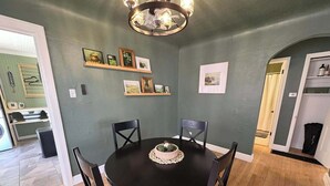 A dining area with a black table and chairs, a chandelier, framed pictures on the wall, and a wooden floor. - The Clover Cottage - Rolla's St.Pat's Themed house near S&T, Acorn Trail & more! (Rolla)