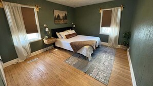 A bedroom with a bed, nightstands, a painting, and a window with curtains. - The Clover Cottage - Rolla's St.Pat's Themed house near S&T, Acorn Trail & more! (Rolla)