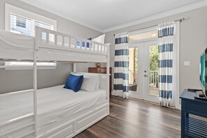 Een slaapkamer met een stapelbed, een raam, een deur die uitkomt op een balkon en een tv op een standaard.