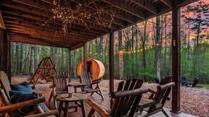 Eine rustikale Holzhütte mit einer Holzdiele, Blockmöbeln und Blick auf einen Wald.